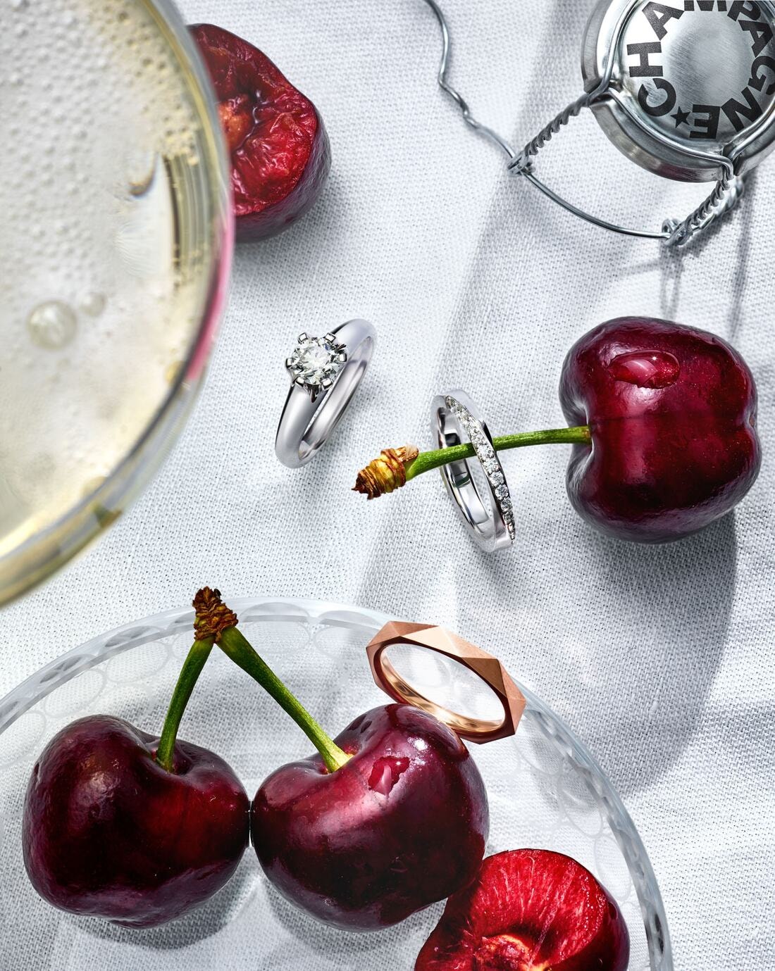 Solitärring und Eheringe zwischen Kirschen und einem Glas Champagner